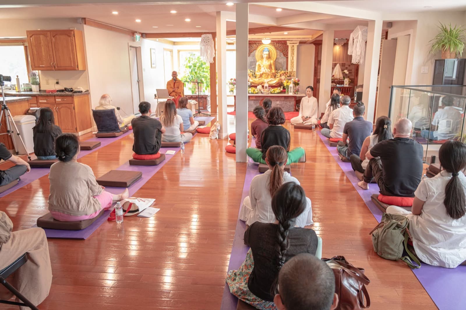 A meditation sitting in the hall: people on cushions, listening to the teacher in front of the Buddha.