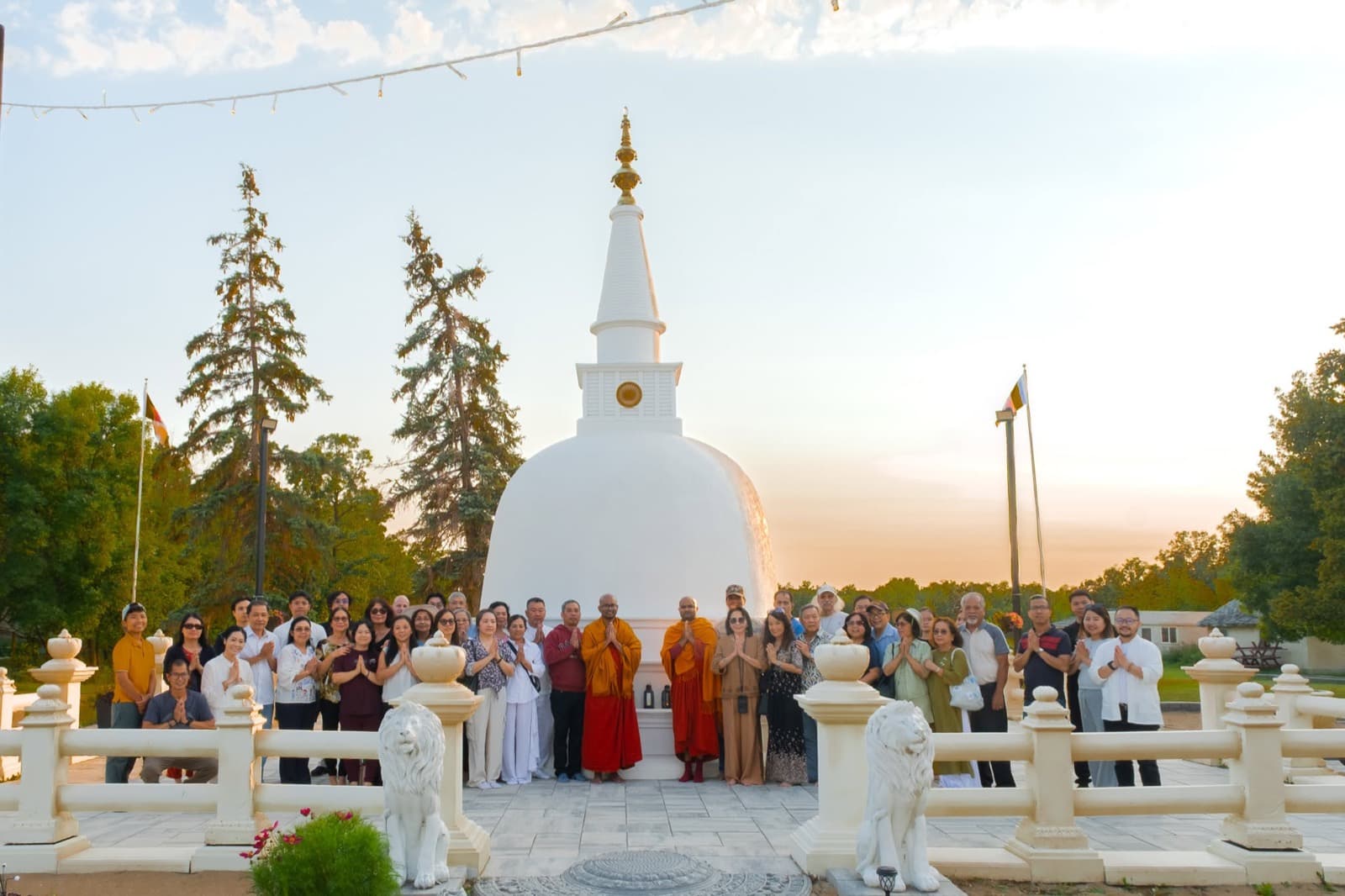 Everyone standing with palms together in front of the white stupa at sunset.