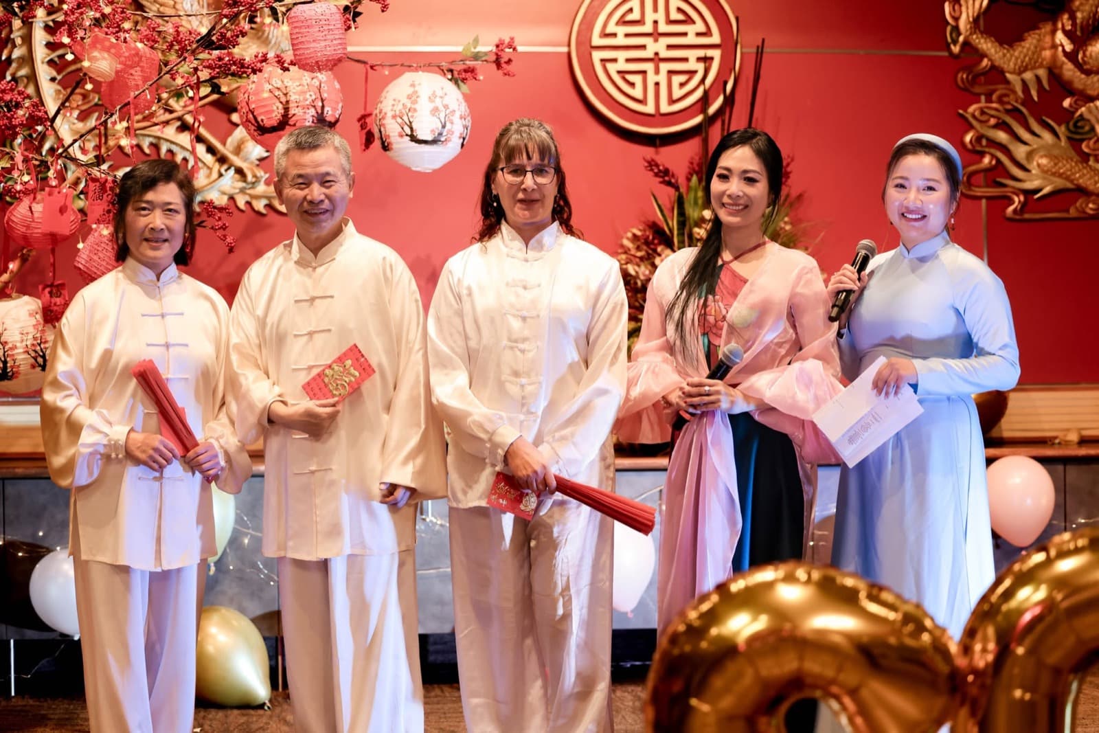 Tai chi performers in white receiving red envelopes from the two hosts on stage.